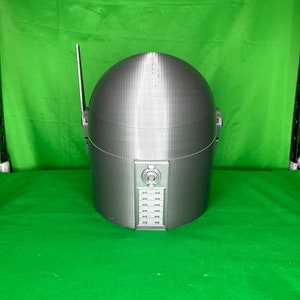 May include: A gray 3D printed helmet with a dome-shaped top and a panel of buttons on the front.