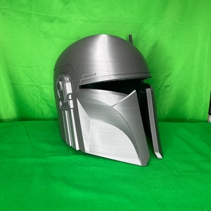 May include: A gray 3D printed helmet with a textured surface and a raised design on the front. The helmet has a visor and a small antenna on top.