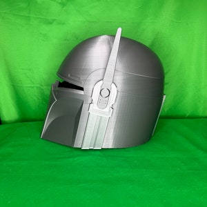 May include: A gray 3D printed helmet with a raised design on the side. The helmet has a pointed fin on top.