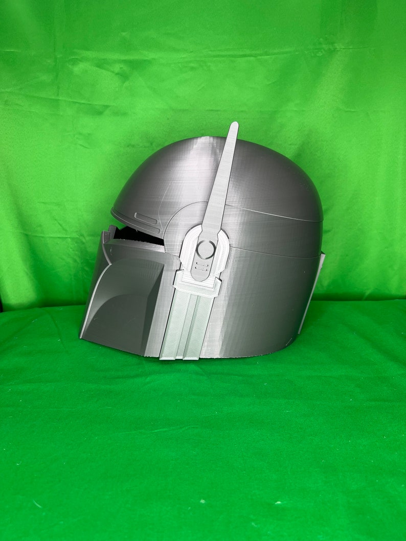 May include: A gray 3D printed helmet with a raised design on the side. The helmet has a pointed fin on top.