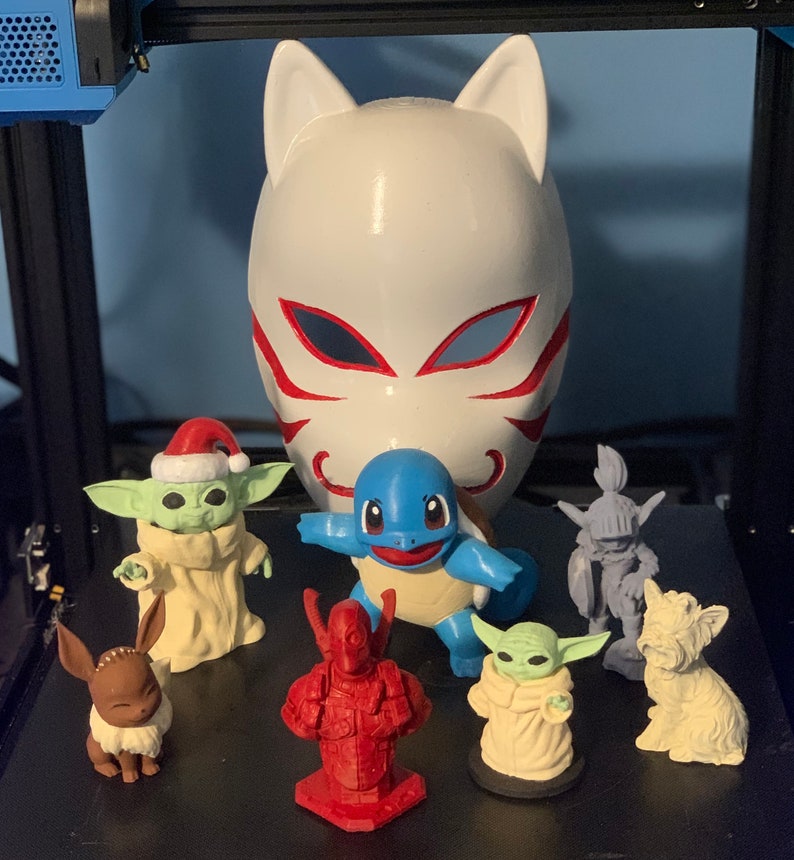 May include: A collection of figurines, including a white fox mask, a blue turtle, a green and white Yoda-like character, a brown and white Eevee, a red and black Deadpool-like character, a white and green Yoda-like character, and a white dog figurine.