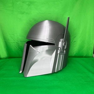 May include: A gray 3D printed helmet with a raised design and a small antenna on top. The helmet is angled to the left and has a textured surface.