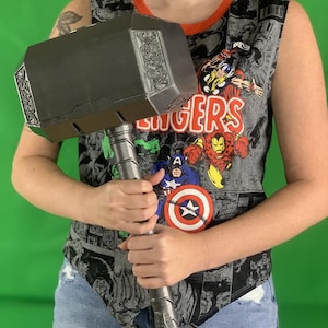 May include: A person holding a large, black, metal hammer with a detailed design on the head. The hammer has a long, silver handle.