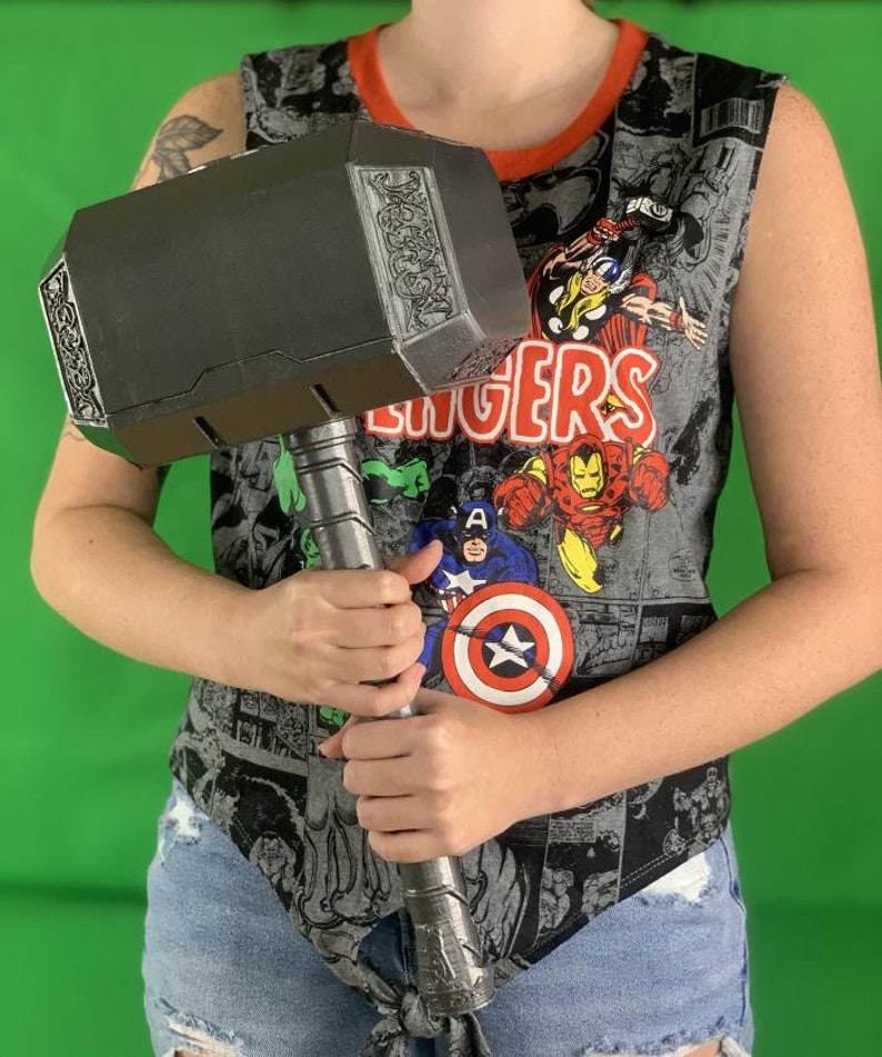May include: A person holding a large, black, metal hammer with a detailed design on the head. The hammer has a long, silver handle.