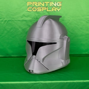 May include: A silver 3D printed helmet with a raised crest and a visor. The helmet is on a green surface.