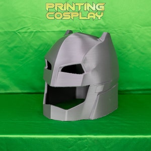 May include: A grey 3D printed Batman helmet with a textured surface. The helmet has a raised design on the top and a black visor.