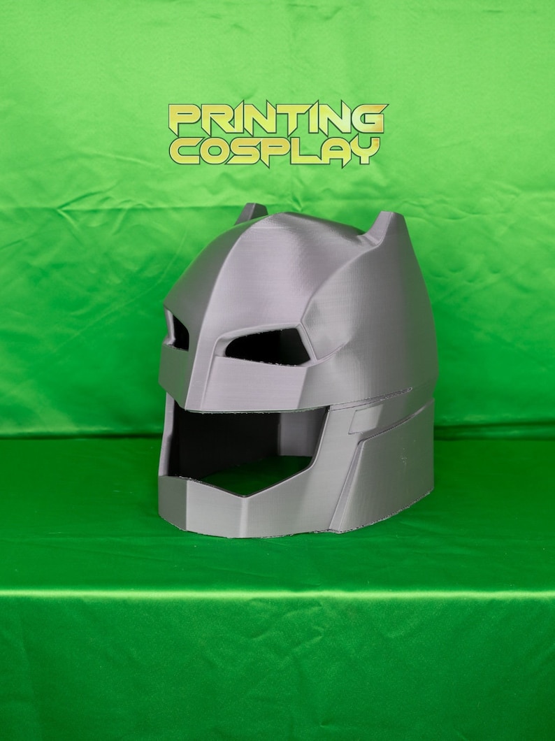 May include: A grey 3D printed Batman helmet with a textured surface. The helmet has a raised design on the top and a black visor.