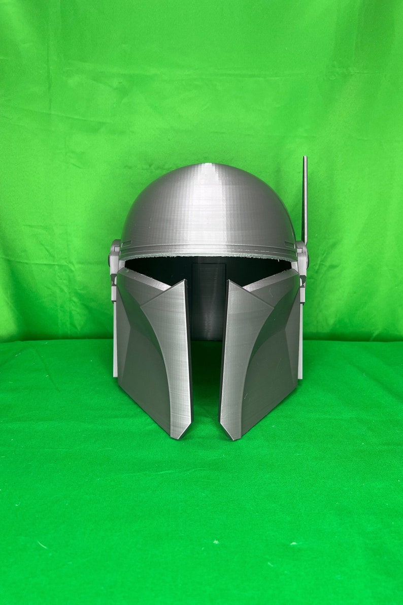 May include: A gray 3D printed helmet with a raised design. The helmet has a pointed top and a visor that is closed.