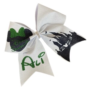 May include: White glitter cheer bow with green and black accents. Features a Minnie Mouse silhouette, the name "Ali" in green, and a black castle design with the year "2023". A rhinestone band is at the center.