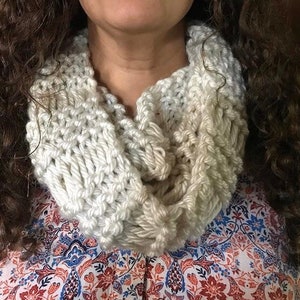 May include: A white knitted infinity scarf with a gradient pattern. The scarf is made of a soft, chunky yarn and is perfect for keeping warm in the winter.