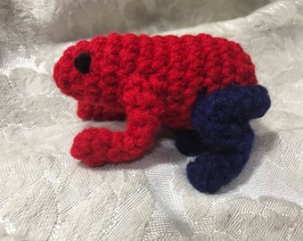May include: A crocheted red and blue frog toy. The frog has a black eye and a blue tail.