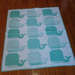 May include: A white quilt with a teal whale pattern. The whales are arranged in rows and are outlined in white. The quilt is made of cotton fabric and is quilted with a simple stitch.