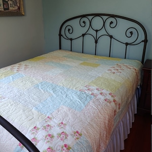 May include: A white, blue, and yellow patchwork quilt with a floral pattern on a bed with a black metal headboard.