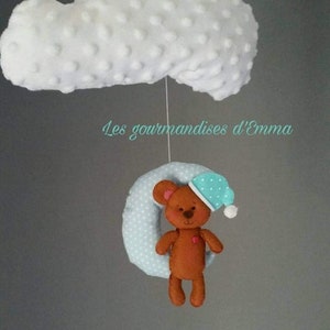 May include: A handmade baby mobile featuring a white cloud with a textured surface, a light blue polka-dot ring, and a brown teddy bear wearing a blue sleep cap. The text "Les gourmandises d'Emma" is visible.