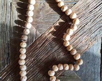 May include: A string of light brown wooden beads with intricate carvings. The beads are strung together with a brown cord and are arranged in a circular shape.