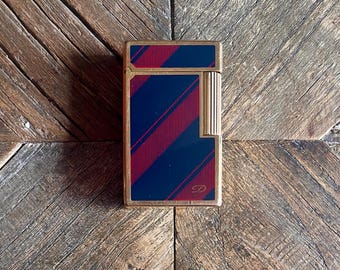 May include: A gold-toned lighter with a black and red striped design. The lighter has a gold trim and a small gold logo on the front.