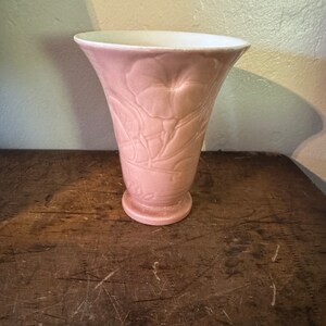 May include: A pink ceramic vase with a floral design. The vase has a wide mouth and a narrow base.