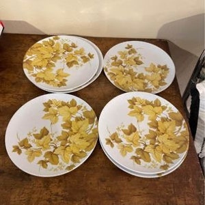 May include: Set of four white ceramic dinner plates with a floral design featuring yellow and brown leaves.