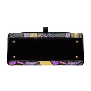 May include: Black handbag with a patchwork design featuring purple, yellow, and gray squares. The bag has a black base with gold-colored feet and a top handle. The patchwork pattern is reminiscent of a quilt.