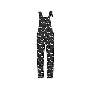 Puede incluir: Pantalón de peto negro con estampado de murciélago blanco. El peto tiene tirantes ajustables y cierre de botón.