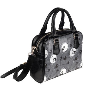 K&ouml;nnte beinhalten: Schwarze Handtasche mit Schultergurt. Die Tasche hat ein grau-wei&szlig;es Muster mit einem sich wiederholenden Bild von Jack Skellington aus Nightmare Before Christmas.