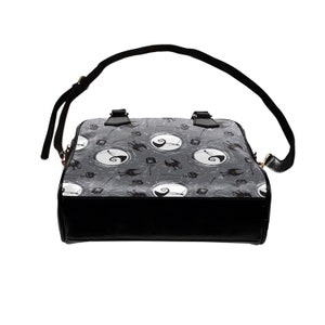 K&ouml;nnte beinhalten: Schwarze und graue Handtasche mit einem sich wiederholenden Muster von Jack Skellingtons Gesicht und einem Halbmond. Die Tasche hat einen oberen Griff und einen Schultergurt.