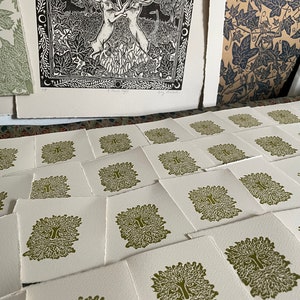 May include: A collection of art prints featuring a Green Man design and a black and white image of two hares. The Green Man prints are in olive green ink on white paper. The hare print is framed with leaves and moons.