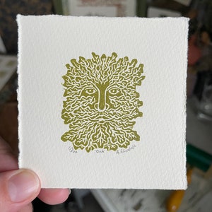 May include: A square, off-white print featuring a stylized green face with a leafy beard and crown. The print is labeled "Oak" and numbered 1/300, with the artist's signature. The print has a deckled edge.