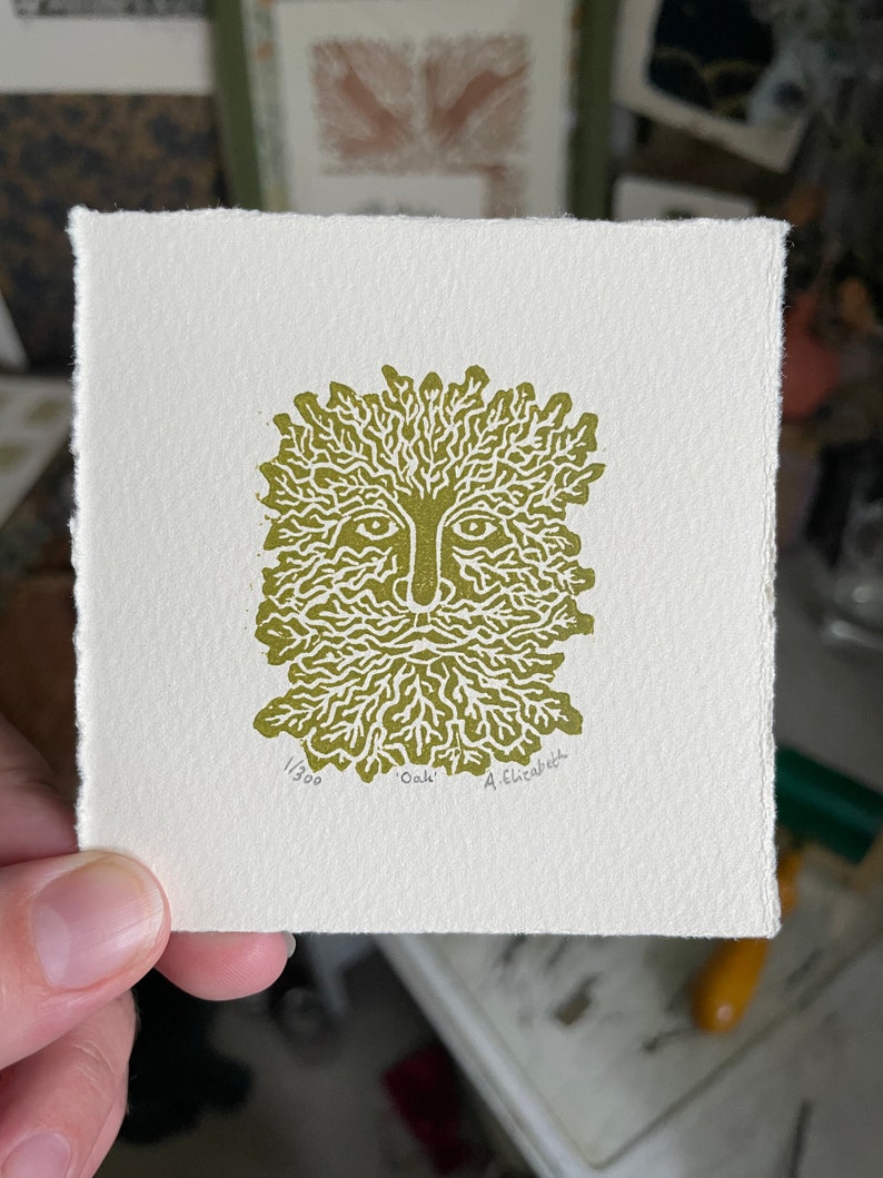 May include: A square, off-white print featuring a stylized green face with a leafy beard and crown. The print is labeled "Oak" and numbered 1/300, with the artist's signature. The print has a deckled edge.