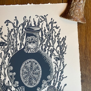 Puede incluir: Un grabado en lin&oacute;leo azul oscuro y blanco titulado "The Witch Bottle" que representa una botella estilizada rodeada de algas marinas, conchas y estrellas de mar. Una peque&ntilde;a campana de cer&aacute;mica marr&oacute;n est&aacute; en la esquina superior derecha.