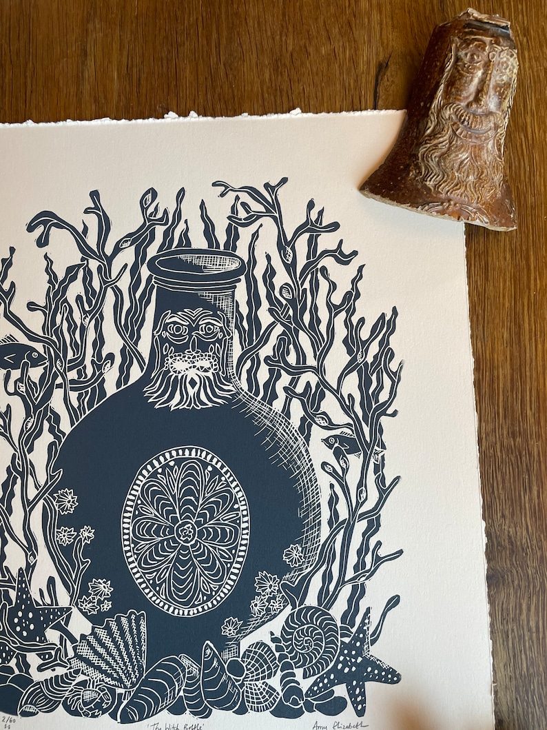 Puede incluir: Un grabado en lin&oacute;leo azul oscuro y blanco titulado "The Witch Bottle" que representa una botella estilizada rodeada de algas marinas, conchas y estrellas de mar. Una peque&ntilde;a campana de cer&aacute;mica marr&oacute;n est&aacute; en la esquina superior derecha.