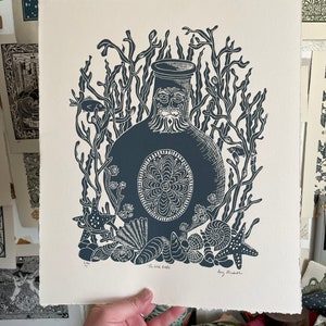 Puede incluir: Una impresi&oacute;n azul oscuro de una botella con una cara, rodeada de algas marinas, conchas y estrellas de mar. La impresi&oacute;n est&aacute; sobre papel color crema. El texto "The Wild Bottle" est&aacute; en la parte inferior.