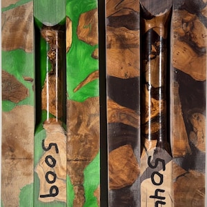 May include: Two rectangular wood and resin turning blanks. The left blank features bright green resin with natural wood burl inclusions and the number 5009. The right blank features dark charcoal resin with natural wood burl inclusions and the number 5044.