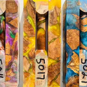 May include: Three rectangular blocks made of natural wood burl and colored resin. The left block features purple and green swirls, the center block has bright yellow resin, and the right block contains blue resin. Each block is marked with numbers 5016, 5017, and 5027.