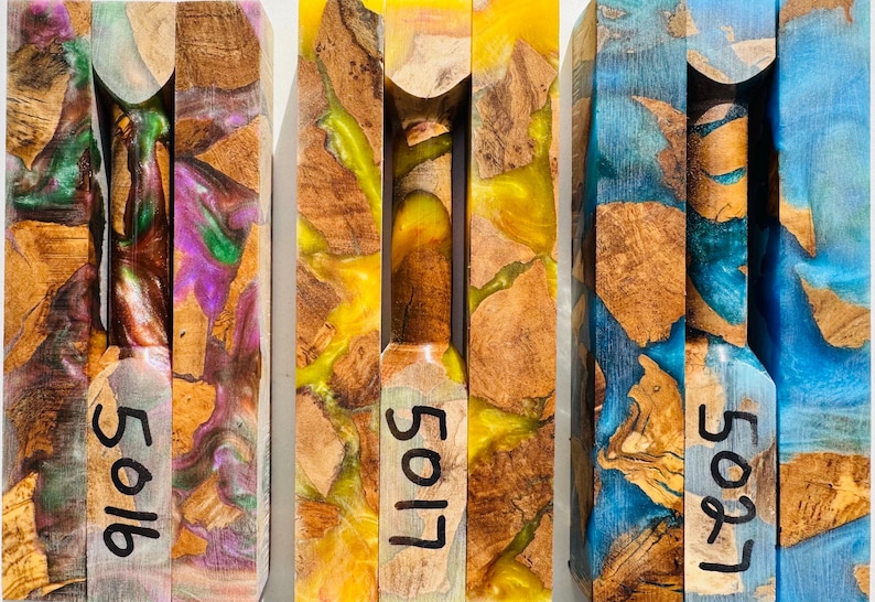 May include: Three rectangular blocks made of natural wood burl and colored resin. The left block features purple and green swirls, the center block has bright yellow resin, and the right block contains blue resin. Each block is marked with numbers 5016, 5017, and 5027.