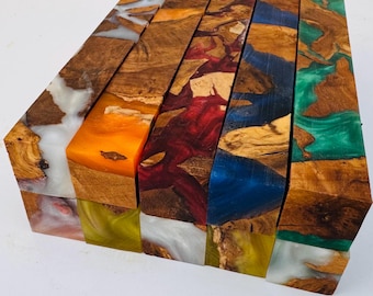 May include: A collection of rectangular wood and resin turning blanks arranged in a row. Each block features a unique combination of natural brown burl wood grain and vibrant, semi-translucent resin in colors including white, orange, red, blue, and green.