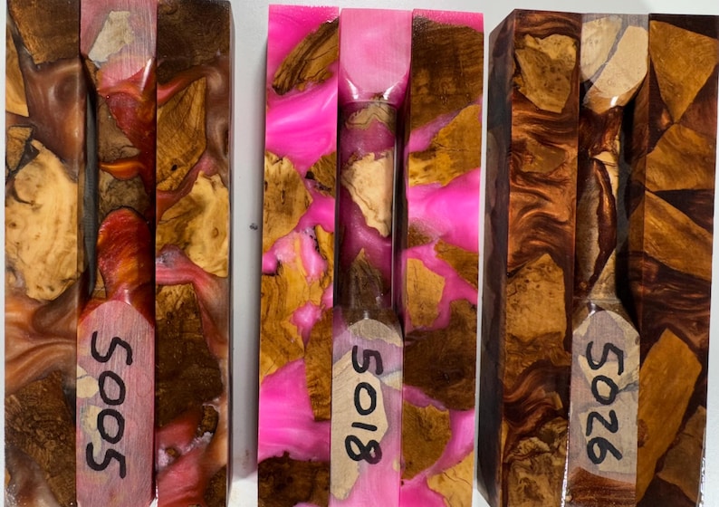 May include: Three rectangular blocks made of wood burl and resin. The left block features orange and brown resin, the center block has bright pink resin, and the right block contains dark brown resin. Each block is marked with the numbers 5005, 5018, or 5026.