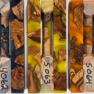 May include: Three rectangular blocks of wood burl encased in colored resin. The left block is black, the center is yellow, and the right is orange. Each block features the handwritten numbers 4062, 5063, and 5064 respectively on the front.