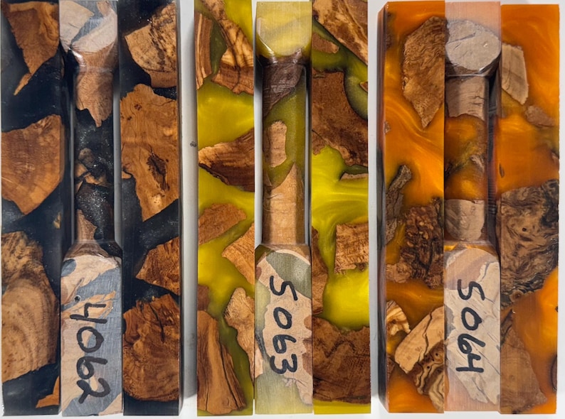 May include: Three rectangular blocks of wood burl encased in colored resin. The left block is black, the center is yellow, and the right is orange. Each block features the handwritten numbers 4062, 5063, and 5064 respectively on the front.