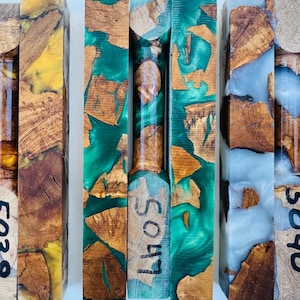 May include: Three rectangular pen blanks made of natural wood burl pieces encased in colored resin. The left blank features yellow resin, the center features green resin, and the right features white resin. Each blank is marked with numbers 5038, 5047, and 5040.