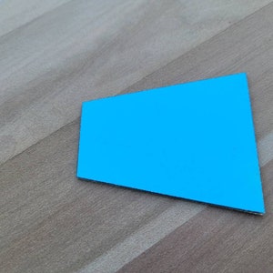 May include: A bright blue paper shape resembling a trapezoid or a slightly skewed rectangle, lying flat on a woodgrain surface.