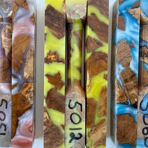 May include: Three rectangular blocks of burl wood encased in colored resin. The left block features pinkish-white resin and is marked 5051. The center block has bright yellow resin and is marked 5012. The right block has blue resin and is marked 5060.