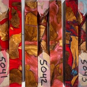 May include: Three rectangular blocks of wood and resin composite. The first block is marked 5041 with red resin, the second is marked 5042 with pink resin, and the third is marked 5043 with blue and red resin. Each block features natural wood burl pieces.