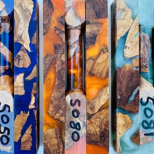 May include: Three rectangular wood and resin turning blanks featuring natural wood burl fragments suspended in vibrant blue, orange, and light green resin. Each blank is marked with black handwritten numbers 5050, 5080, and 5081 respectively.