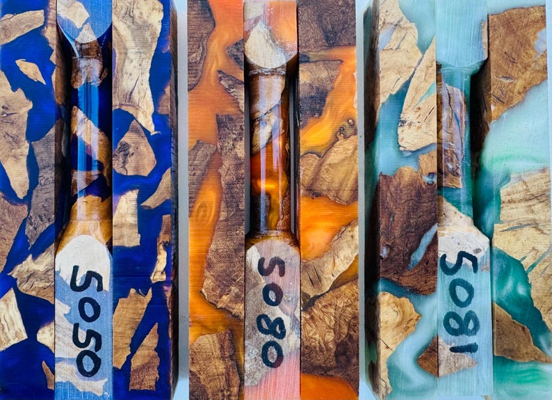 May include: Three rectangular wood and resin turning blanks featuring natural wood burl fragments suspended in vibrant blue, orange, and light green resin. Each blank is marked with black handwritten numbers 5050, 5080, and 5081 respectively.