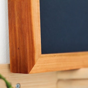 May include: Close-up of a wooden frame with a dark blue background. The frame is made of a rich, reddish-brown wood with a natural grain pattern.