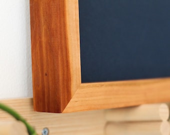 May include: Close-up of a wooden frame with a dark blue background. The frame is made of a rich, reddish-brown wood with a natural grain pattern.