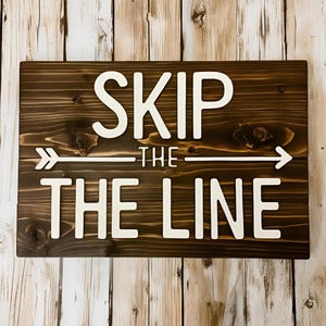 May include: A rectangular wooden sign with the words "SKIP THE LINE" in white, raised lettering. A white arrow points to the right. The sign is stained a dark brown color.