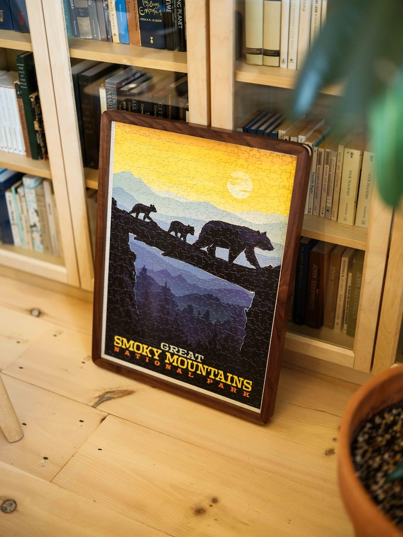 May include: A framed jigsaw puzzle depicting the Great Smoky Mountains National Park. The image shows three bears on a ridge with a sunset. The frame is made of dark wood. The puzzle is likely 50 cm x 70 cm.