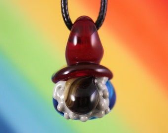 May include: A glass pendant necklace featuring a red, white, and blue gnome with a black and brown striped beard. The gnome is wearing a red hat.